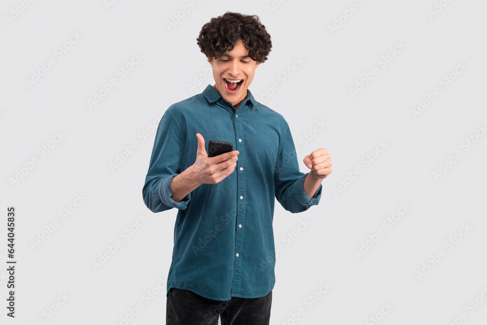Poster man using smartphone and making winner gesture over white background