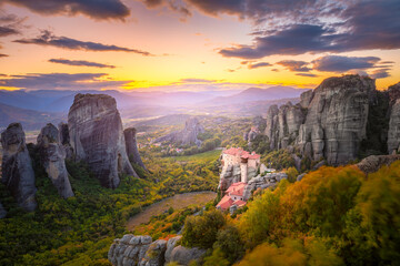 Panoramic landscape of Meteora, Greece at romantic sundown time with real sun and sunset sky. Meteora - incredible sandstone rock formations.  The Meteora area is on UNESCO World Heritage.