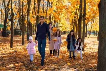Naklejka na ściany i meble portrait of a family with children in an autumn city park, happy people walking together, playing with yellow leaves, beautiful nature, bright sunny day
