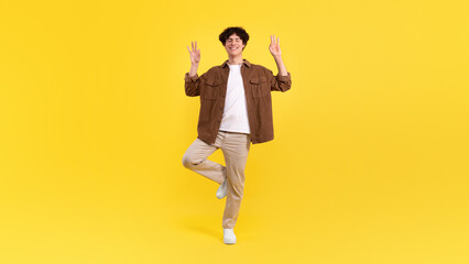 Fototapeta na wymiar Man standing on one leg making om gesture, yellow background