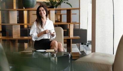 Middle-aged business woman drinking coffee or tea in office lobby. Successful businesswoman having rest after meeting