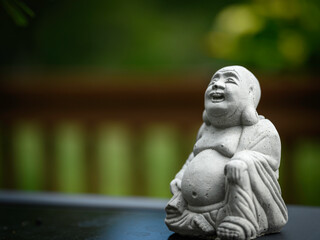 Laughing Budha, Zen garden statue, with big belly and chin, on the blurred green nature background,...
