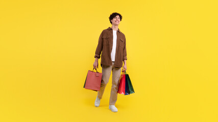 Guy after shopping many packages bags posing on yellow background
