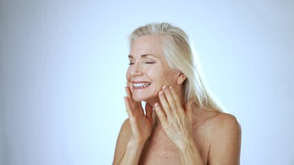 Happy 50s, 60s middle aged mature woman touching face skin pampering in mirror. Old healthy dry skin care beauty concept, cosmetics and anti age plastic surgery.