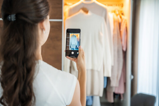 Young woman taking photos of old unwanted clothes for sale in smartphone app
