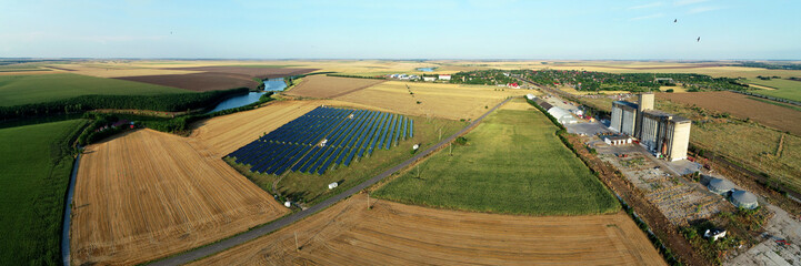 Aerial view of a big solar panel field plant, lake and agriculture field. Landscape with plant that produce electricity from the sunlight. Eco green energy industry.
