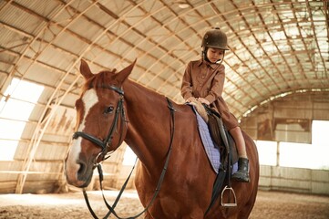 Riding the animal. Cute little girl is with horse indoors