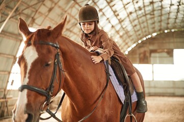 Riding the animal. Cute little girl is with horse indoors