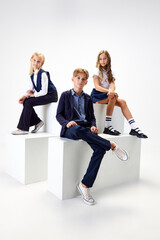 Group of stylish children, boys and girls, pupils in school uniform standing against white studio background. Concept of childhood, school, education, fashion, style. Copy space for ad