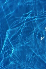 Blue water with ripples on the surface. Defocus blurred transparent blue colored clear calm water surface texture with splashes and bubbles. Water waves with shining pattern texture background.