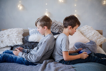 Two boys sitting with their backs turned to each other and playing games on their phones against...