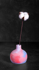 Multicolored vase with a branch of cotton on a black background, front view, copy space,  low key. Home decor.