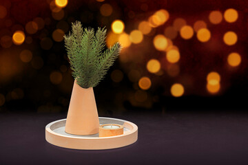 Festive composition with fir branches in a vase and candlestick on a tray on a black background with Christmas lights.  Front view, copy space.