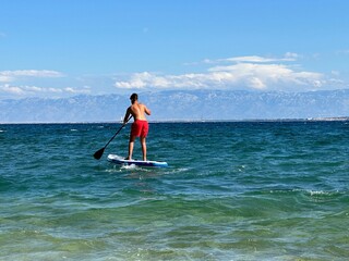 A man floats on a surfboard. Concept: Water sports, entertainment at sea. A young guy stands on a surfboard in the sea.