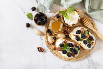Keto diet sandwiches, snack. Sweet bruschetta with cheese and berries blackberry ricotta and honey on marble table. Healthy breakfast toasts. View from above. Copy space.