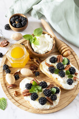 Healthy breakfast toasts. Keto diet sandwiches. Keto snack. Sweet bruschetta with cheese and berries blackberry ricotta and honey on marble table.