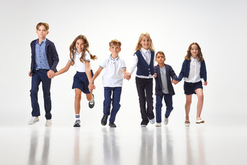Group of stylish children, boys and girls, pupils in school uniform running against white studio background. Classmates. Concept of childhood, school, education, fashion, style. Copy space for ad