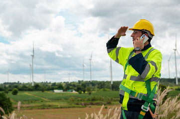 A smart engineer with protective helmet on head, using smartphone at electrical turbines field