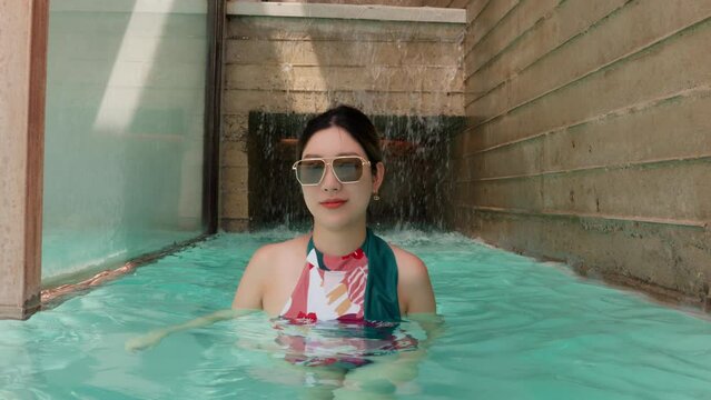 A glamorous sight as a girl, sporting swimwear and sunglasses, strides through a sunlit swimming pool. Her stylish and the shimmering water create an ambiance of sunny-day elegance and relaxation.
