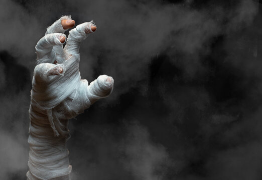 Halloween background.Bandaged zombie hand on dark smoky background.Halloween design.Copy space.