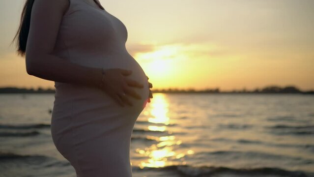 A pregnant woman stands by the water, gently cares