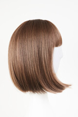Naklejka premium Natural looking dark brunet wig on white mannequin head. Middle length brown hair on the plastic wig holder isolated on white background, side view.