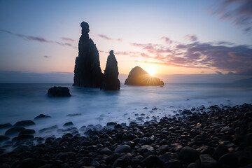 Beautiful sunrise by the popular rock at Ribeira de Janela, Madeira, Portugal. Jagged island in Atlantic Ocean lit by the morning light. - 644080657