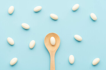 White soft gelatin capsules with wooden spoon on light blue background. Concept of probiotic...