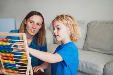 Mother and son playing together with abacus inside home living room - Family leisure and study time - Motherhood concept