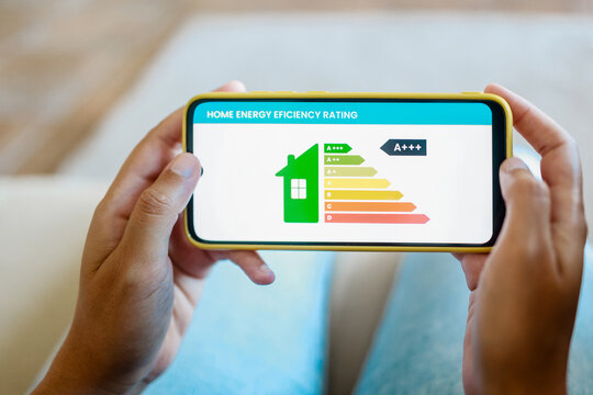 Home energy performance: Hands hold mobile phone looking at house efficiency rating app - Environment and electricity concept