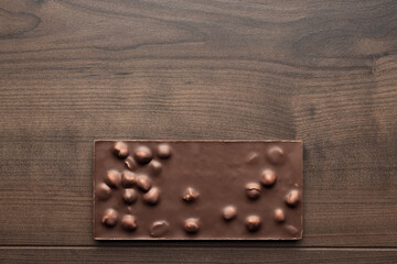 Chocolate bar with whole hazelnuts on brown table. Flat lay image of chocolate on wooden background with copy space.