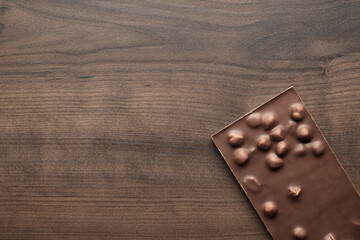 Chocolate bar with whole hazelnuts on brown table. Top view photo of chocolate on wooden background with copy space.