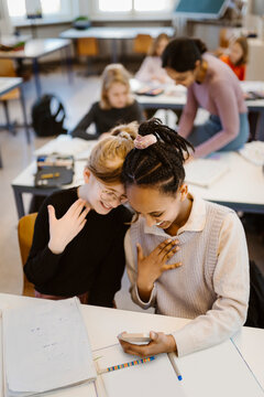 High angle view of schoolgirls gesturing while using smart phone sitting at desk in classroom