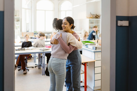 Schoolgirl embracing female teacher standing in classroom