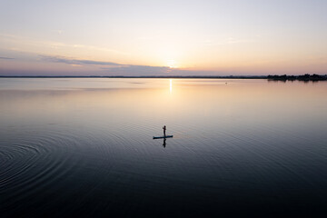 Girl paddling on SUP board on beautiful lake during sunset or sunrise standing up paddle boarding morning adventure in lake district. top view, aerial view,