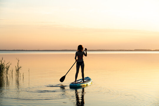 Sports girl on board for glanders surfing. young slender woman floats on a board with a paddle. Surfing. Summer fun on the water. Healthy lifestyle. Woman stand up paddle boarding SUP on calm water