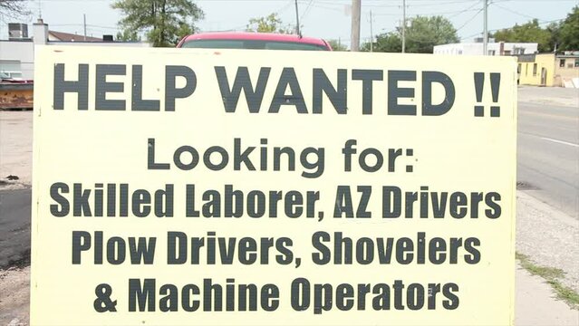 help wanted looking for skilled laborer az drivers plow drivers shovelers and machine operators sign with car vehicle traffic and big truck passing in background, yellow sign with black writing