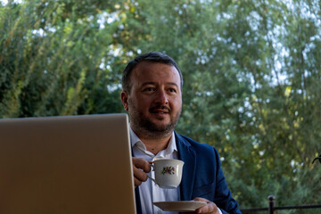 Fototapeta premium a man with laptop and coffee in a hand smile, mature business man in an outdoor ambition working ,blue coat suit,multiracial asian, successful businessman.