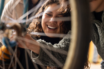 Happy female technician seen through bicycle wheel spokes at recycling center