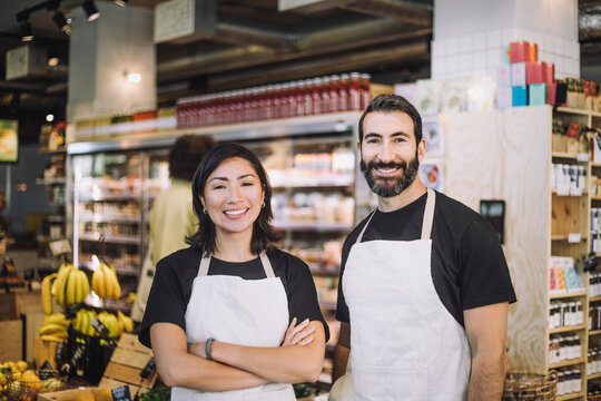Portrait of smiling multiracial male and female retail clerks wearing aprons standing at grocery store