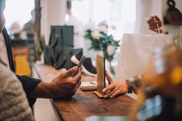 Cropped hands with smart phone and QR code at checkout in boutique