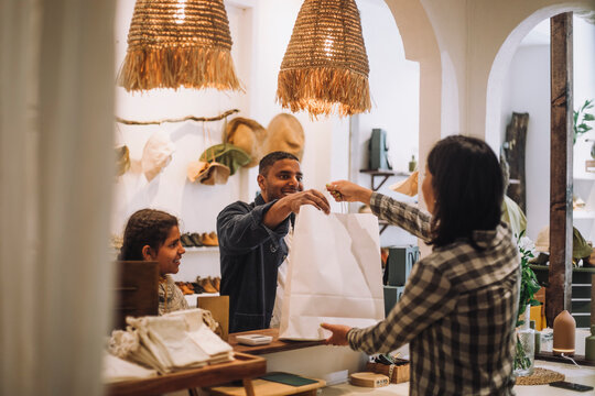 Saleswoman giving bag to male customer at checkout in clothing boutique