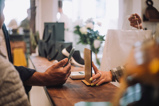 Cropped hands with smart phone and QR code at checkout in boutique