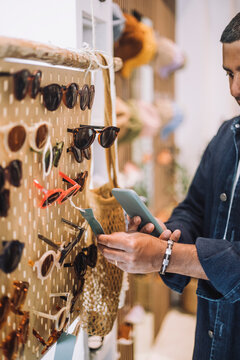 Man photographing label on sunglasses at rack in fashion store