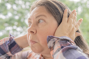 mature caucasian woman 50 years holding hand to sore ears, close up female face with facial...