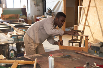 Side view portrait of young black man building wooden furniture in carpentry workshop, copy space