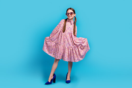 Full body photo of small smiling cute schoolgirl kid posing model wear pink dress new stilettos sunglass isolated on blue color background