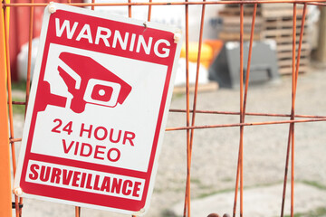 warning 24 hour video surveillance sign on orange locked gate for dirt yard parking lot with...