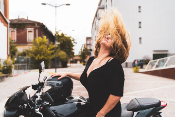 Fototapeta na wymiar middle aged biker woman tossing her blond hair back riding modern black motorcycle