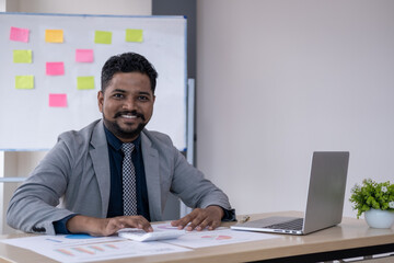 Young handsome happy man working in office on laptop and smiling